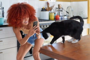 Happy woman taking a photo picture with her mobile cell phone of her pet cat at home kitchen