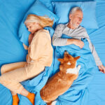 A dog sleeping on a sleeping couple in their bed