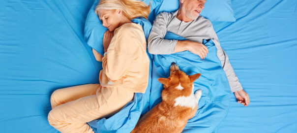 A dog sleeping on a sleeping couple in their bed